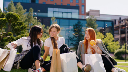 Good looking ladies office workers after work they laying down on the garden enjoy the sun one of lady take a fruit to eat they discussing together background modern building architecture