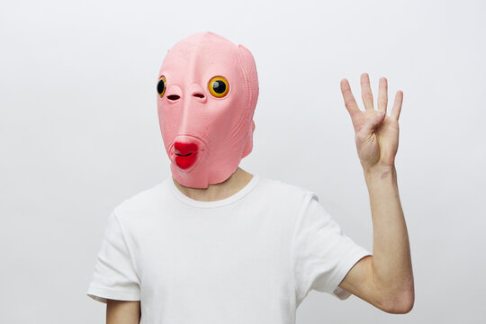 a man in a funny pink mask in the form of a fish on a light background shows four fingers
