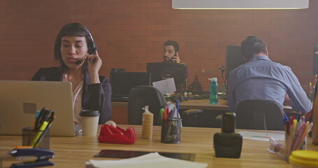 Group of people working inside corporate office at night. Young men and women employees in front of computers. Workspace and businesspeople concept. Millennials staff at work