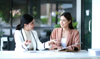 Two young Asian businesswoman discuss investment project working and planning strategy. Business people talking together with laptop computer at office.