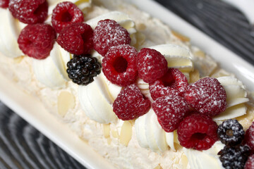 Meringue roll with mascarpone cream. Garnished with raspberries and almond petals. Close-up.