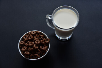 A glass of milk on a black background and chocolate corn rings. Delicious breakfast of cornflakes and milk.
