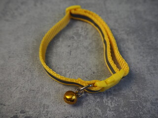 a small yellow collar with a bell lies on a gray background. view from above. collar for cats and puppies