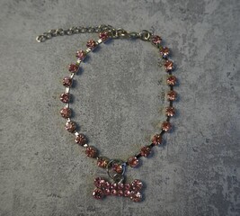 a metal necklace with pink stones and a dog bone pendant lies on a gray background.  top view. ...