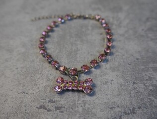 a metal necklace with pink stones and a dog bone pendant lies on a gray background.  side view.  small dog collar