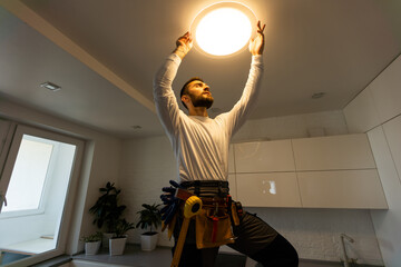 Electrician worker installation electric lamps light inside apartment. Construction decoration...