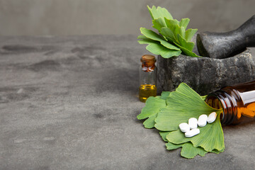 Bottle of pills, essential oil and ginkgo leaves on grey. Traditional, herbal medicine and...