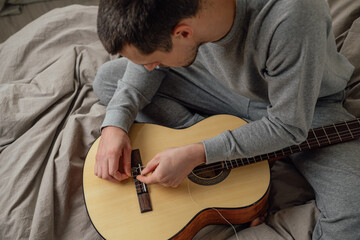 The guy pulls a new string on an acoustic guitar. Musical instrument.