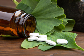 Bottle of pills and ginkgo biloba leaves in mortar on wooden background. Traditional, herbal...