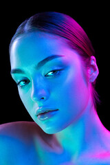 Closeup young beautiful woman with well-kept skin and sophisticated facial features isolated over dark background in purple neon light.