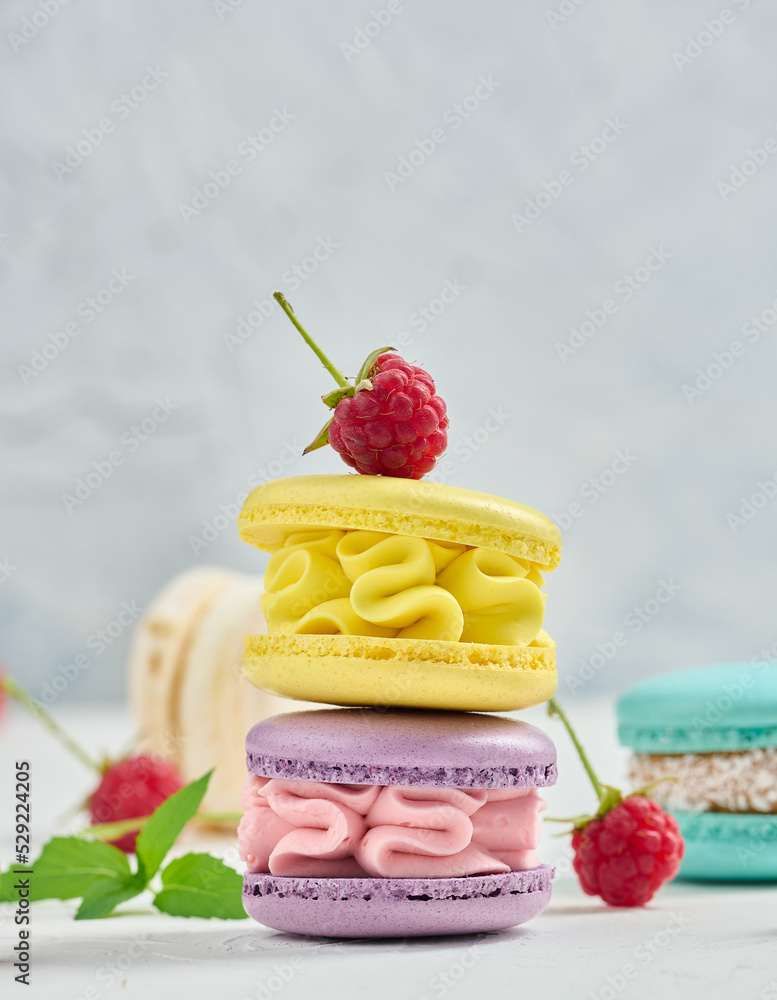 Poster a stack of multicolored macaroons and red raspberries on a white background.