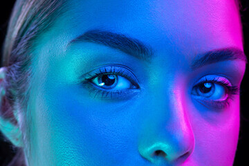 Close up eyes of beautiful young girl looking at camera in pink neon light. Concept of cosmetics, makeup, natural and eco treatment, skin care.