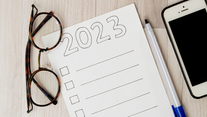 To-do list with squares for ticks and lines for text, glasses, pen and phone on a wooden background