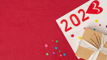 the number 2023 next to the gift box on a red background with confetti, new year