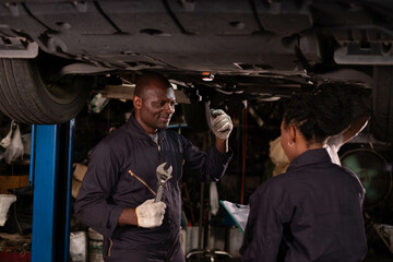 African american  Two mechanics - man examining car engine. Auto mechanic working in garage.Car Mechanic Detailed Vehicle Inspection. Auto Service Center Theme.
