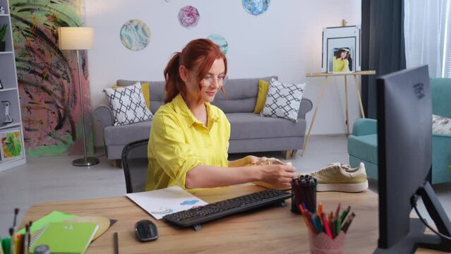 charming female designer in glasses takes sneakers to update the design and sensible consumption of used things while sitting at home in a modern room