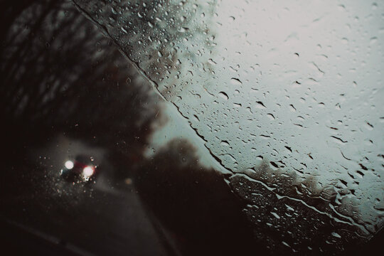 parabrisas con gotas de lluvia en una carretera con un auto desenfocado por delante