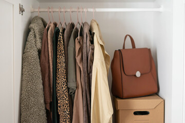Capsule basic wardrobe in a white wardrobe in brown and beige colors. Autumn clothes on hangers.