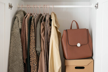 Capsule basic wardrobe in a white wardrobe in brown and beige colors. Autumn clothes on hangers.