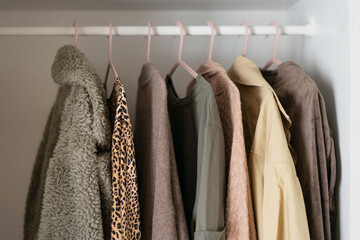 Capsule basic wardrobe in a white wardrobe in brown and beige colors. Autumn clothes on hangers.