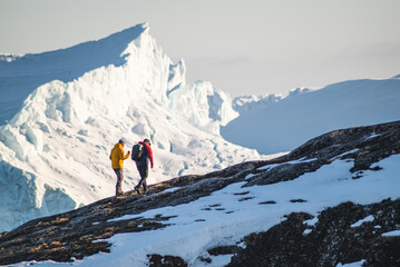 Tourists hiking on hills next to icebergs in winter, next to Ilulissat Icefiord in Greenland on...