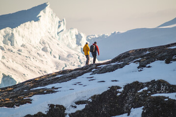 Tourists hiking on hills next to icebergs in winter, next to Ilulissat Icefiord in Greenland on...