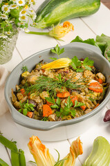 Oven baked vegetables with herbs in a baking dish on a white wooden background