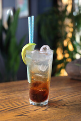 Long island iced tea, long drink. Cocktail with alcohol, cola, ice cubes, lime, on a wooden table, selective focus.