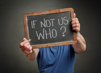 If not us who? A question in white chalk on a slate blackboard held by a man, call for action, motivation  and communication concept