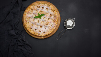 Round baked apple pie on a black table. View from above