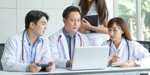 Young asian intern, young male and female doctor sitting with Senior Doctor talk and discuss using laptop in office.