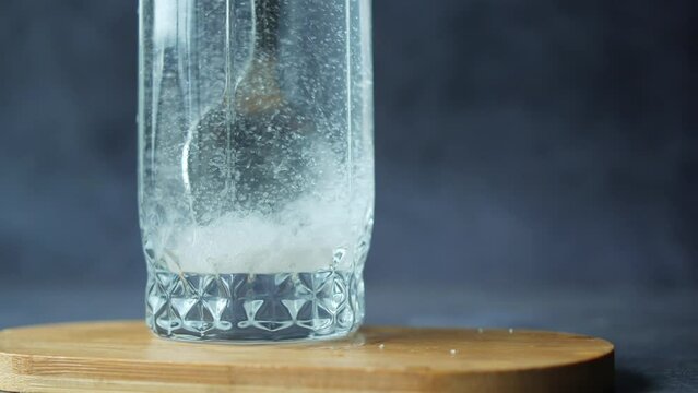 pouring white sugar in a glass of water on table 