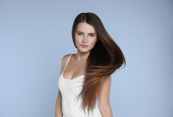 Young woman with strong healthy hair on light blue background