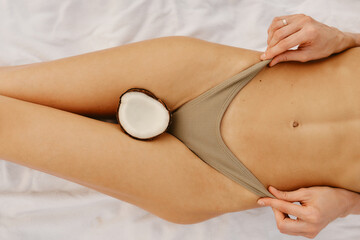 Coconut on the body of a woman in a bikini on the beach.