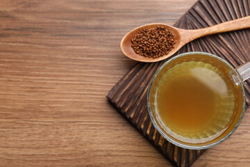 Cup of aromatic buckwheat tea and granules on wooden table, top view. Space for text