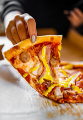 woman hand hold slice of Pizza with Mozzarella cheese, ham, tomato sauce, pepper, pepperoni, sausage and mustard sauce