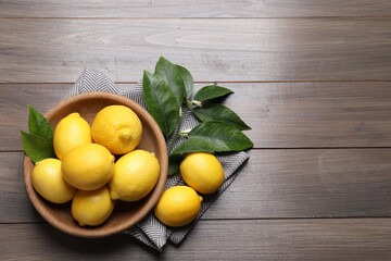 Many fresh ripe lemons with green leaves on wooden table, flat lay. Space for text
