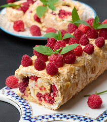 Baked meringue roll with cream and fresh red raspberry on a black wooden board