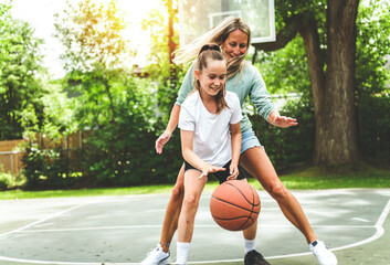 Mother and little daughter play basketball outside