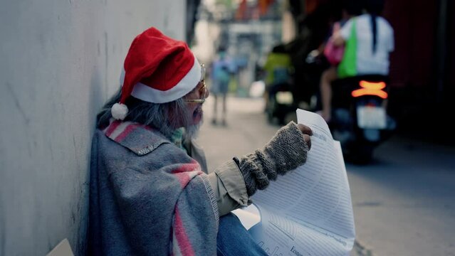4K, Asian homeless old man read a newspaper in the corner of the building to look for a job, a man who waits for hope and help because there is no home and no job stay hungry