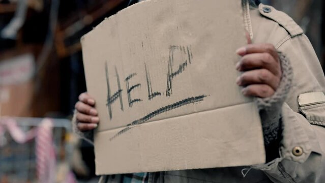 4K, Close-up of a paper sign with a message for help in the hand of a dirty old man standing by the roadside. homeless seek help from those who pass by with hope.