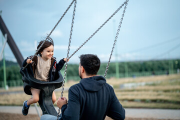 Obraz premium Dad and son swing on a swing. Happy family. The father spends time with the children, the father walks with the child in the summer in the park