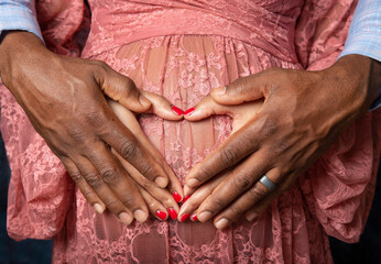 Hands of young African American black couple forming a heart shape on the pregnant belly of the...