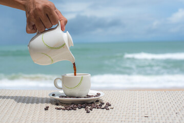 Hands  pouring coffee from pot into cup. near the Indian ocean. Spa relaxing time at the beach with white sand. Hot beverage near the sea