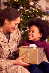 Fototapeta na wymiar American Female Soldier In Uniform Home On Leave For Christmas Giving Daughter Present