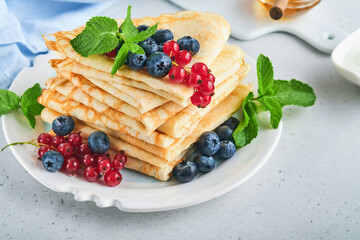 Pancakes. Stack of crepes or thin pancakes with berries, blueberries, red currants, raspberries and honey for breakfast. Homemade breakfast. Copy space. Selective focus.