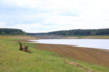 Fototapeta na wymiar A dried up empty reservoir and dam during a summer heatwave, low rainfall and drought in Saxony, Germany, Talsperre Lehnmuehle