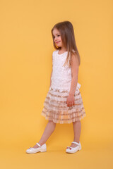 Studio shot of a  young  smiling girl wearing white dress against yellow background  in studio