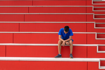 A young teen boy in a blue T-shirt sits upset about something on a red ladder in the street
