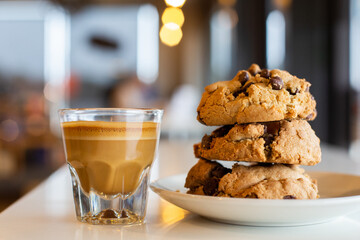 Espresso drink and stack of chocolate chip cookies on a cafe table.